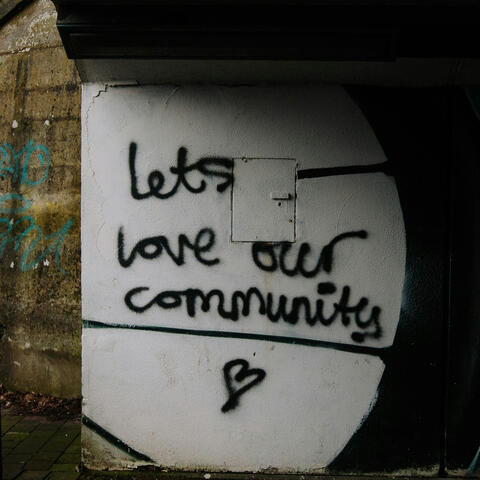 black graffiti on a white wall reads "lets love our community" with a small heart shape beneath the words.